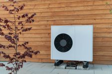 Energy-efficient outdoor AC unit mounted on a modern wooden house. Smart cooling solution for residential comfort and climate control.